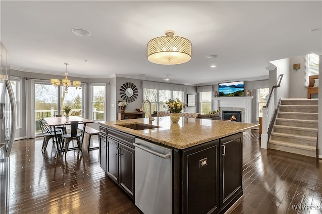 kitchen featuring a sink, appliances with stainless steel finishes, a warm lit fireplace, a chandelier, and ornamental molding