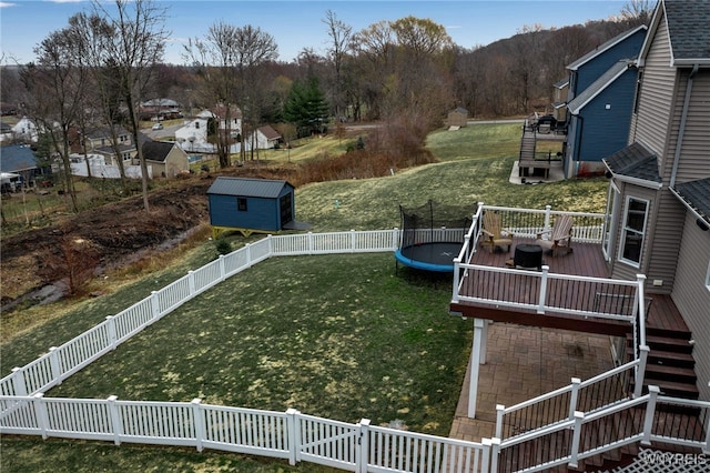 view of yard featuring a trampoline, a wooden deck, stairs, and a storage unit