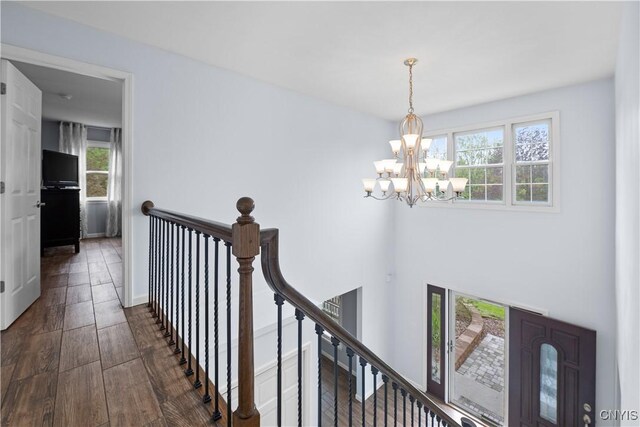 hall with healthy amount of natural light, a chandelier, an upstairs landing, and dark wood finished floors