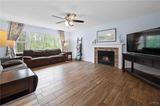 living room with ceiling fan, wood finished floors, a lit fireplace, and baseboards