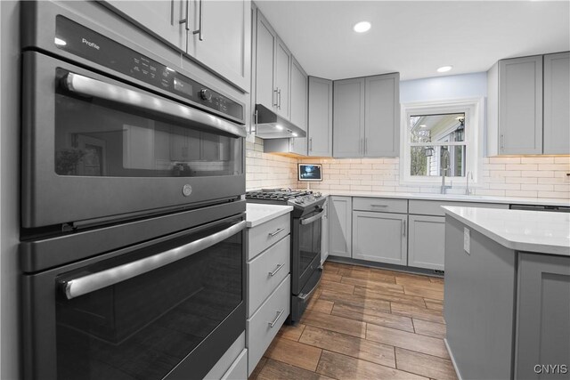 kitchen with gas stove, gray cabinetry, double oven, dark wood-type flooring, and recessed lighting