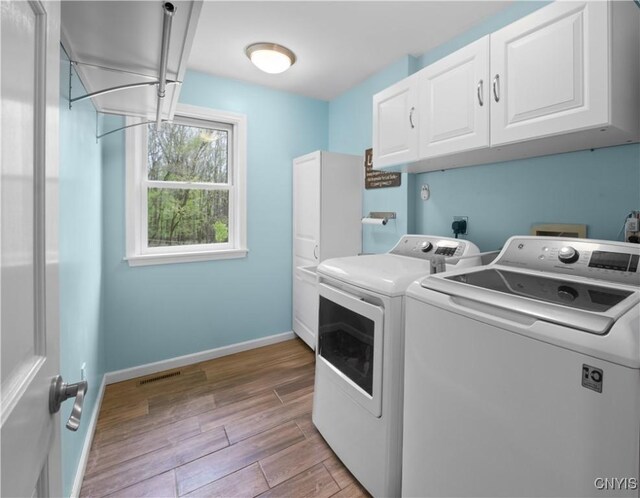 clothes washing area featuring cabinet space, independent washer and dryer, light wood-type flooring, and baseboards