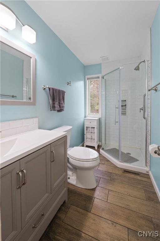 bathroom featuring wood finished floors, a shower stall, toilet, and vanity