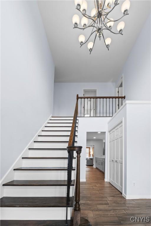 staircase with wood finished floors, a chandelier, baseboards, and a towering ceiling