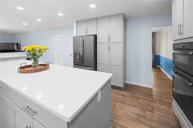 kitchen featuring stainless steel fridge, wood finished floors, recessed lighting, baseboards, and light countertops