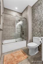 full bath with toilet, bath / shower combo with glass door, and wallpapered walls