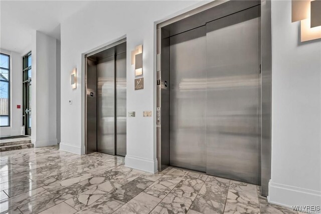hall featuring elevator, marble finish flooring, and baseboards