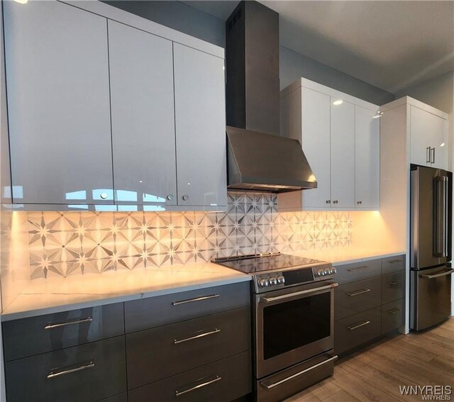 kitchen with appliances with stainless steel finishes, wall chimney range hood, wood finished floors, light countertops, and white cabinets