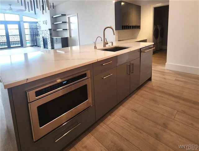 kitchen featuring a sink, light wood-type flooring, stainless steel appliances, a fireplace, and washer and dryer