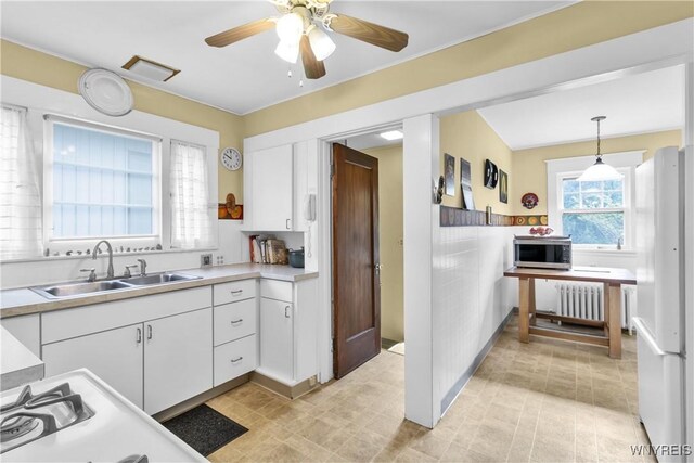 kitchen featuring stainless steel microwave, freestanding refrigerator, radiator, a sink, and white cabinets
