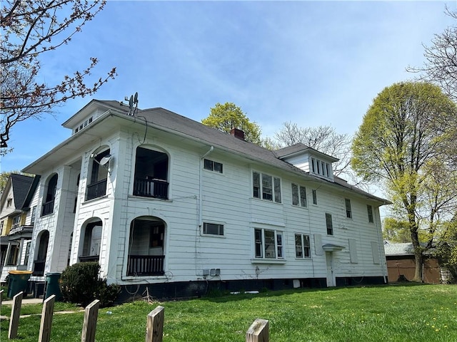 rear view of house with a yard, a balcony, and a chimney