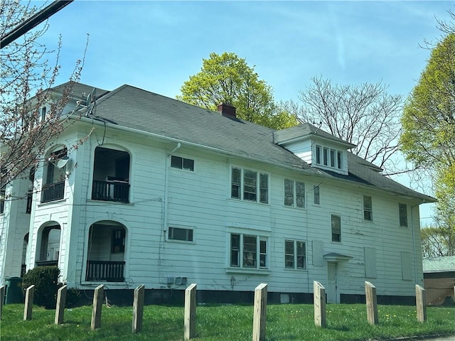 view of property exterior with a balcony, a chimney, and a yard