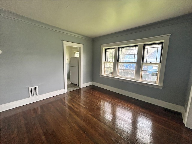 unfurnished bedroom with freestanding refrigerator, dark wood-style floors, baseboards, and ensuite bath