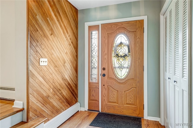foyer entrance with baseboard heating, wood walls, baseboards, a baseboard radiator, and light wood-type flooring
