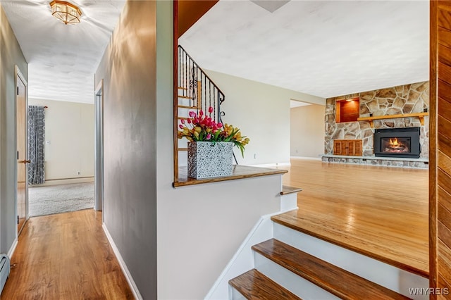stairway with wood finished floors, baseboards, a stone fireplace, and baseboard heating