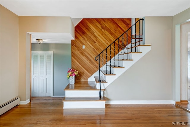 stairs featuring a baseboard heating unit, wood finished floors, baseboards, and wood walls