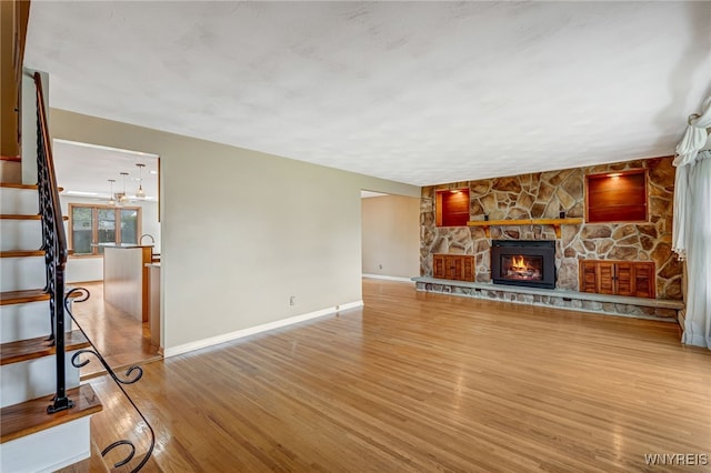 unfurnished living room featuring wood finished floors, a fireplace, baseboards, and stairs