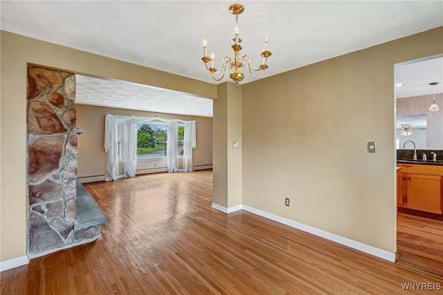 unfurnished living room featuring light wood finished floors, baseboards, a chandelier, and a sink