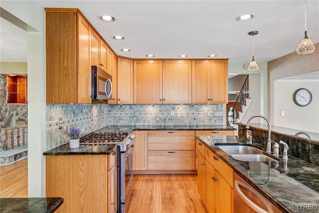 kitchen with stainless steel appliances, a sink, dark stone countertops, light wood-style flooring, and recessed lighting