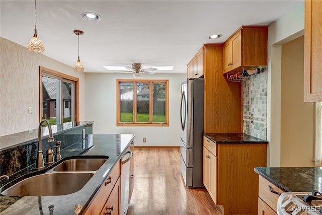 kitchen featuring appliances with stainless steel finishes, a sink, ceiling fan, a skylight, and dark stone counters