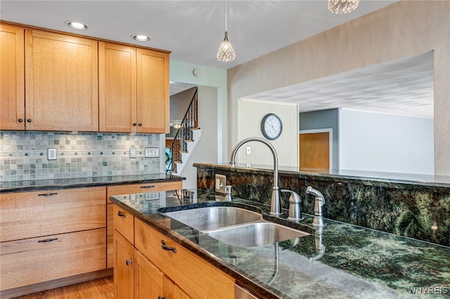 kitchen featuring a sink, dark stone counters, decorative backsplash, decorative light fixtures, and light wood-style floors