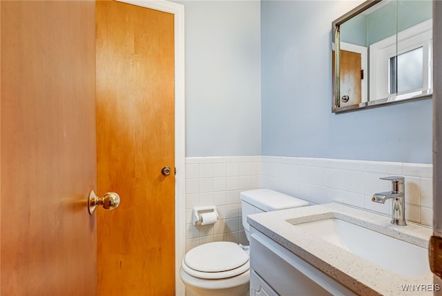 bathroom with tile walls, toilet, a wainscoted wall, and vanity
