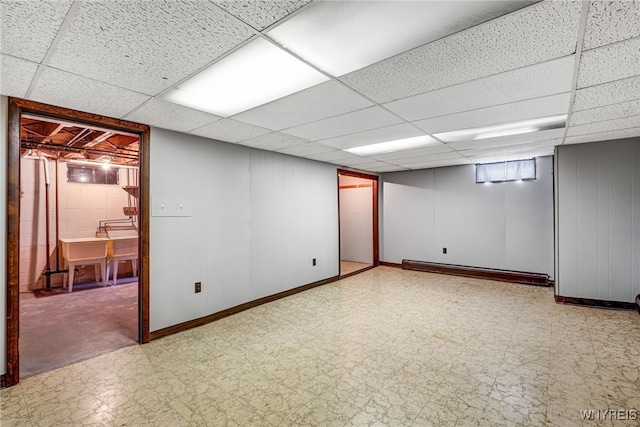 basement with tile patterned floors, baseboard heating, a drop ceiling, baseboards, and a sink