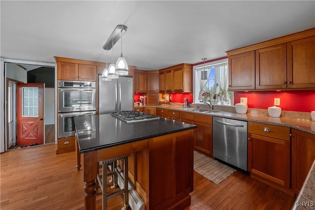 kitchen with stainless steel appliances, a sink, hardwood / wood-style floors, brown cabinetry, and a kitchen bar