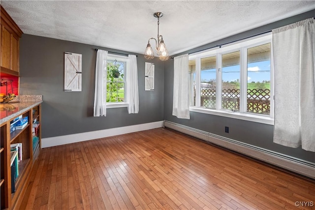 unfurnished dining area with a baseboard radiator, baseboards, a chandelier, wood-type flooring, and a textured ceiling