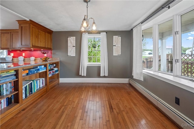 unfurnished dining area featuring a baseboard radiator, baseboards, and light wood-type flooring