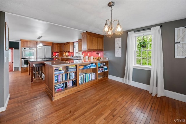 kitchen with appliances with stainless steel finishes, brown cabinets, light wood-style flooring, and baseboards