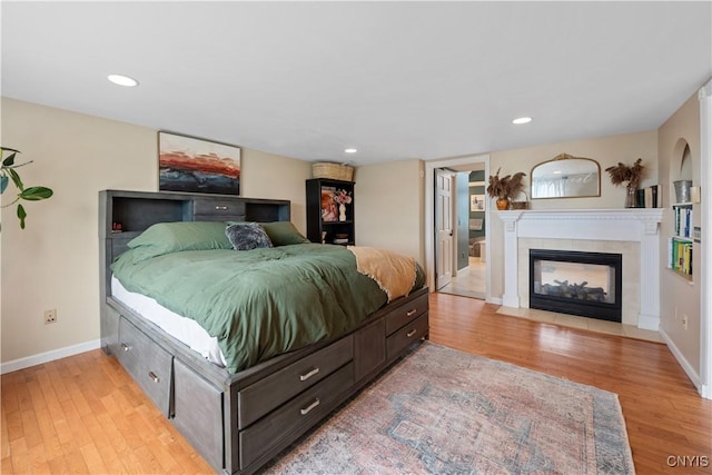 bedroom featuring light wood-type flooring, baseboards, a tile fireplace, and recessed lighting