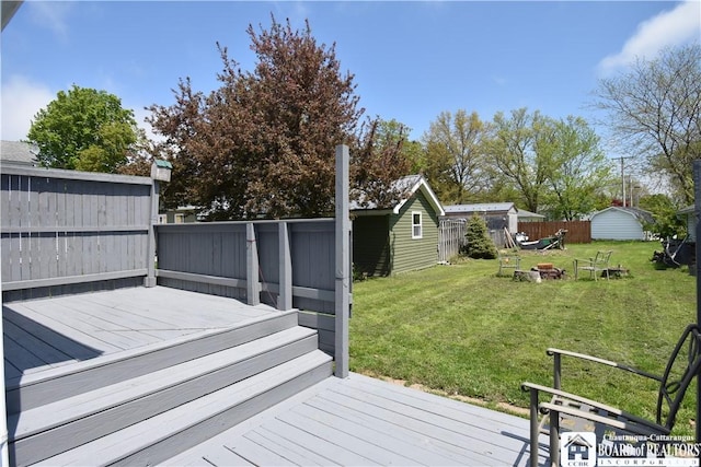 wooden terrace featuring a fire pit, a shed, and an outbuilding