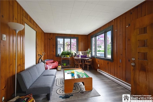 living room featuring a baseboard heating unit, wood walls, and wood finished floors