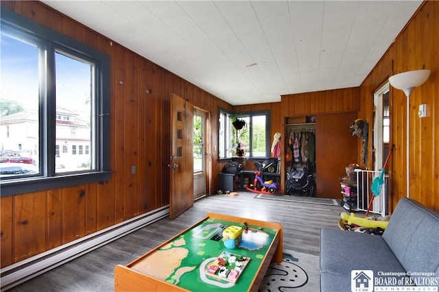 game room featuring a baseboard heating unit, wood walls, and wood finished floors