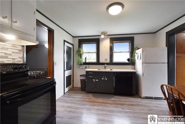 kitchen featuring black appliances, a sink, crown molding, light wood-style flooring, and under cabinet range hood