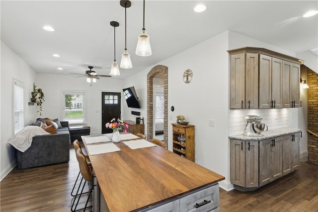 dining room with dark wood finished floors, ceiling fan, recessed lighting, arched walkways, and baseboards