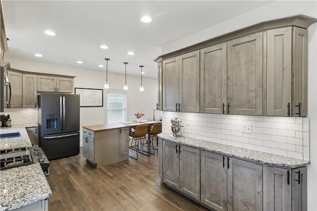 kitchen with fridge with ice dispenser, decorative backsplash, dark wood-type flooring, a center island, and recessed lighting