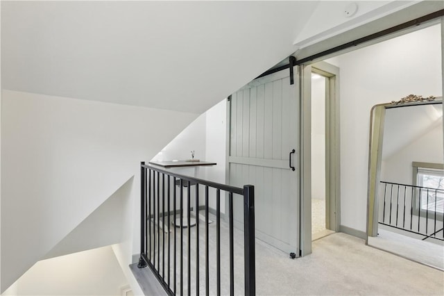 hall featuring an upstairs landing, carpet flooring, a barn door, and baseboards