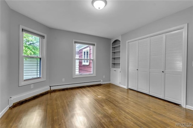 unfurnished bedroom featuring a baseboard radiator, multiple windows, wood finished floors, and a closet