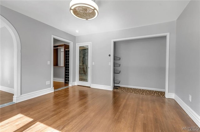 unfurnished room featuring arched walkways, wood finished floors, and baseboards