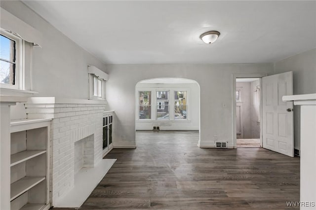 329 Jewett Ave, Buffalo, NY 14214 - unfurnished living room with a brick fireplace, dark wood-type flooring, arched walkways, and baseboards