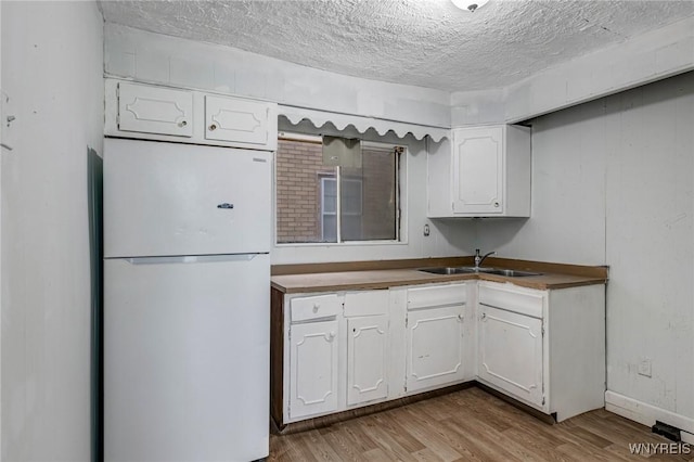 329 Jewett Ave, Buffalo, NY 14214 - kitchen featuring freestanding refrigerator, a sink, white cabinets, light wood finished floors, and a textured ceiling