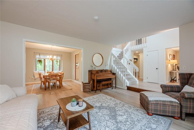 living room with a chandelier, light wood-type flooring, stairway, and baseboards
