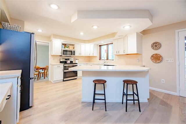 kitchen featuring appliances with stainless steel finishes, a peninsula, a breakfast bar, light wood finished floors, and recessed lighting