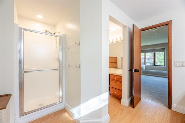 full bath featuring wood finished floors, a shower stall, vanity, and baseboards