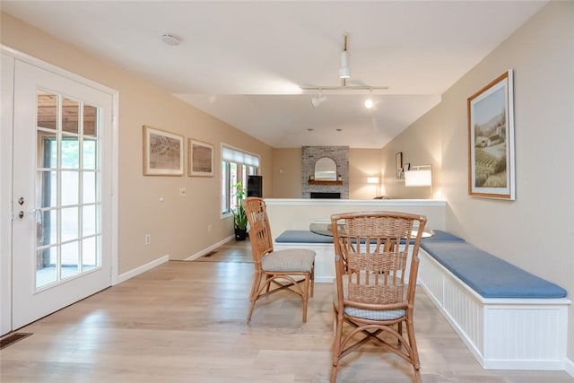 dining room featuring track lighting, light wood finished floors, a fireplace, vaulted ceiling, and baseboards
