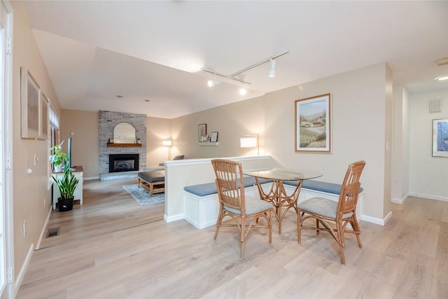dining area with light wood finished floors, track lighting, a large fireplace, and baseboards