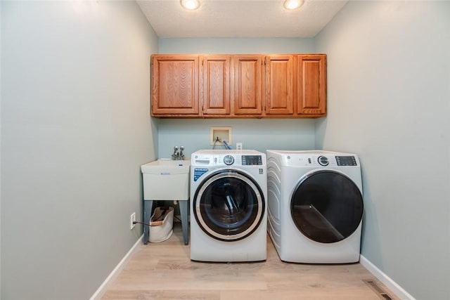 clothes washing area with cabinet space, washer and dryer, light wood-type flooring, and baseboards