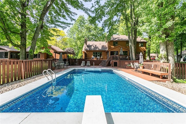 view of pool with a deck, fence, and a diving board